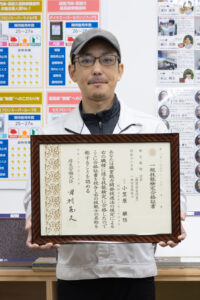 一級塗装技能士の証書を持つ小笠原店長の写真
